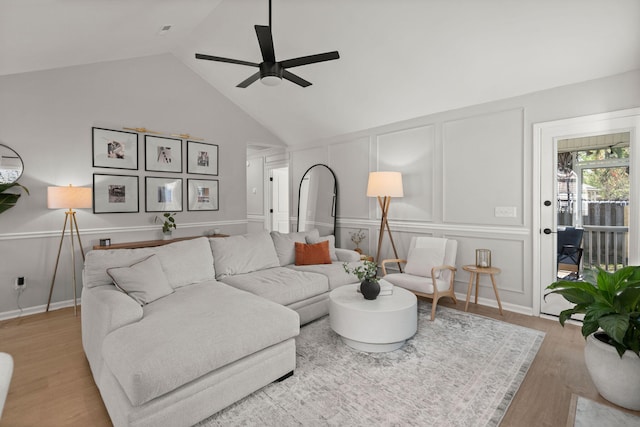 living room with wood finished floors, a decorative wall, a ceiling fan, and high vaulted ceiling