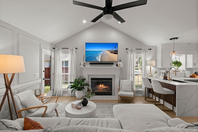 living area with a premium fireplace, lofted ceiling, ceiling fan, and light wood-style flooring