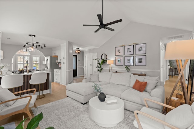 living area featuring visible vents, light wood finished floors, high vaulted ceiling, and ceiling fan with notable chandelier