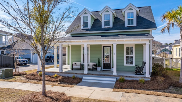 view of front of home with a shingled roof, covered porch, and fence