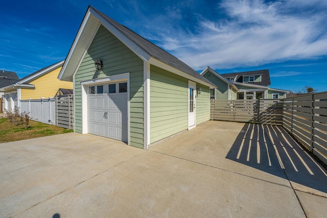 view of side of property featuring a garage, concrete driveway, an outbuilding, and fence