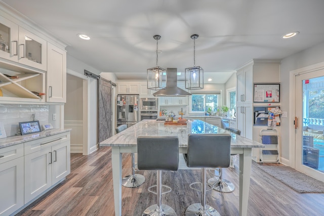 kitchen featuring island range hood, decorative light fixtures, a kitchen island, stainless steel appliances, and a barn door