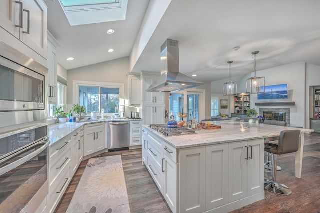 kitchen featuring a spacious island, lofted ceiling with skylight, island exhaust hood, stainless steel appliances, and white cabinets