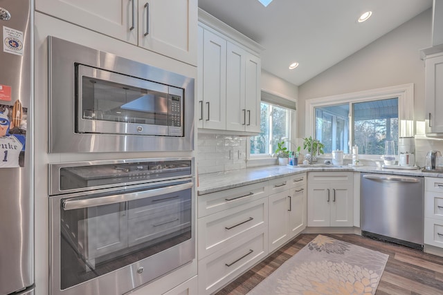 kitchen with vaulted ceiling, white cabinetry, backsplash, stainless steel appliances, and light stone countertops