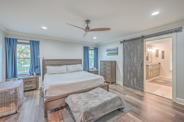 bedroom with ensuite bath, ornamental molding, ceiling fan, a barn door, and hardwood / wood-style floors