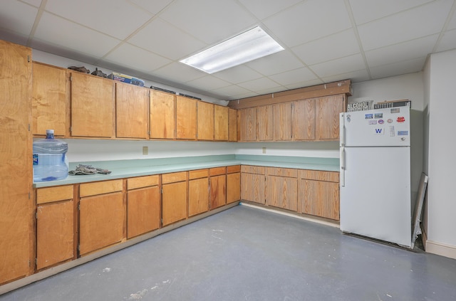 kitchen with concrete floors, white fridge, and a drop ceiling