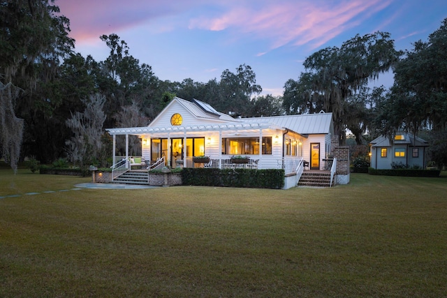 back of house at dusk with a pergola, a lawn, a standing seam roof, and metal roof
