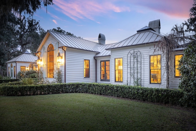 exterior space featuring a yard, a chimney, a standing seam roof, and metal roof