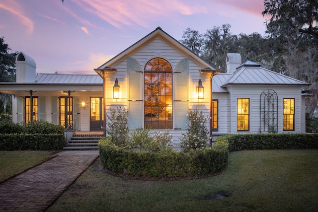 view of front of house featuring a standing seam roof, a front lawn, a chimney, and covered porch