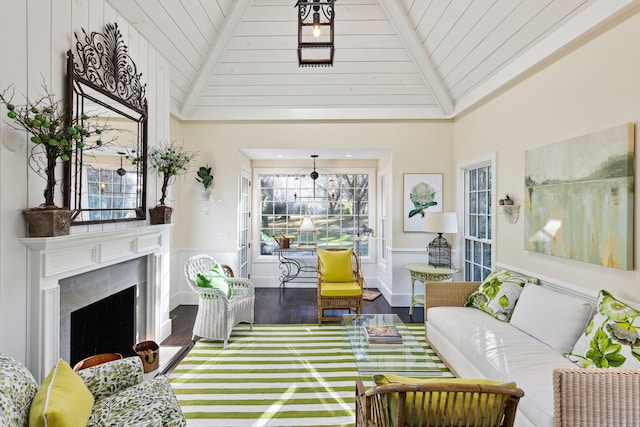 living area featuring a high end fireplace, wood finished floors, a decorative wall, wainscoting, and high vaulted ceiling