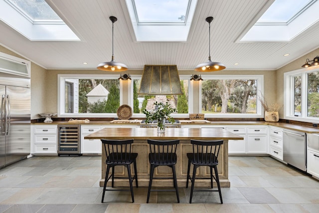 kitchen featuring stainless steel appliances, wine cooler, a skylight, butcher block countertops, and white cabinetry