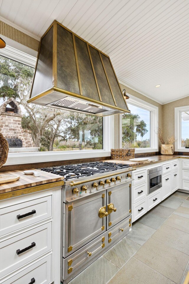 kitchen with custom exhaust hood, white cabinetry, stainless steel microwave, and range with two ovens