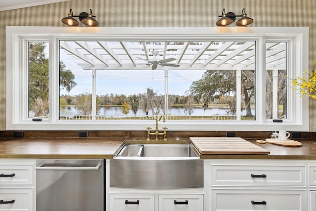 kitchen with white cabinets, stainless steel dishwasher, a sink, a water view, and a ceiling fan