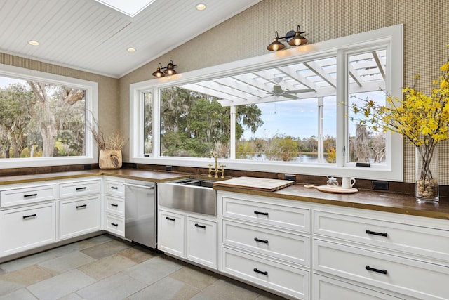 kitchen with vaulted ceiling, a sink, dishwasher, butcher block counters, and white cabinetry