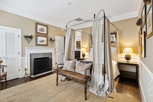 bedroom with hardwood / wood-style floors, a tiled fireplace, and ornamental molding