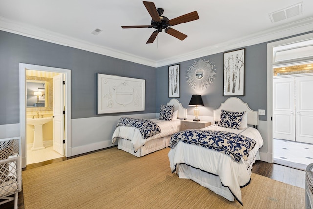 bedroom with wood finished floors, visible vents, ensuite bathroom, and ornamental molding