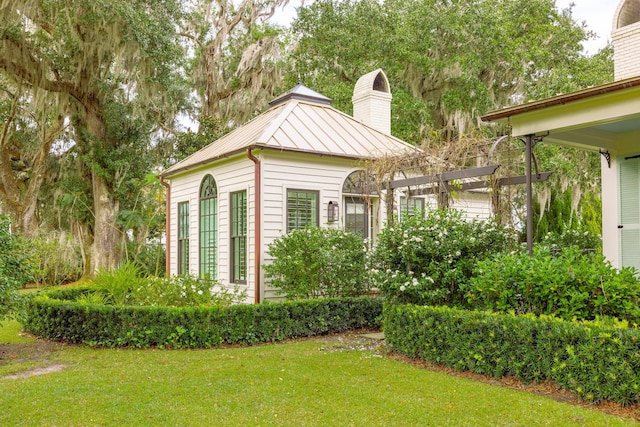 exterior space featuring a standing seam roof, a pergola, a chimney, metal roof, and a lawn