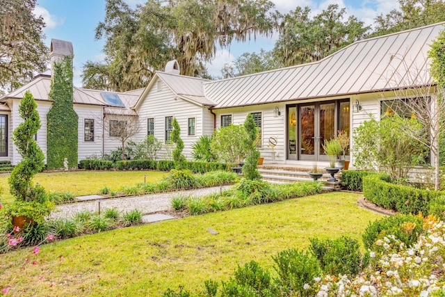 back of house with a chimney, a lawn, french doors, metal roof, and a standing seam roof