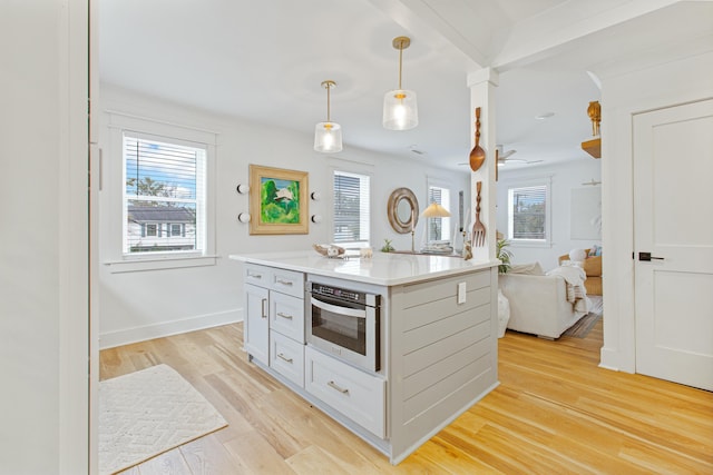 kitchen with white cabinets, oven, decorative light fixtures, and light hardwood / wood-style flooring