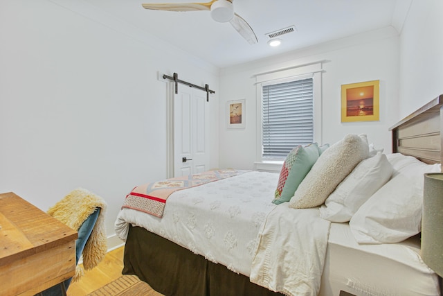 bedroom featuring a barn door, ceiling fan, crown molding, and wood-type flooring