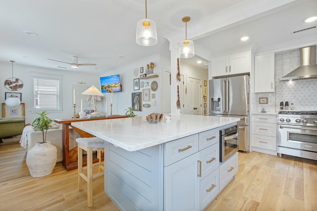 kitchen featuring wall chimney exhaust hood, hanging light fixtures, stainless steel appliances, tasteful backsplash, and white cabinets