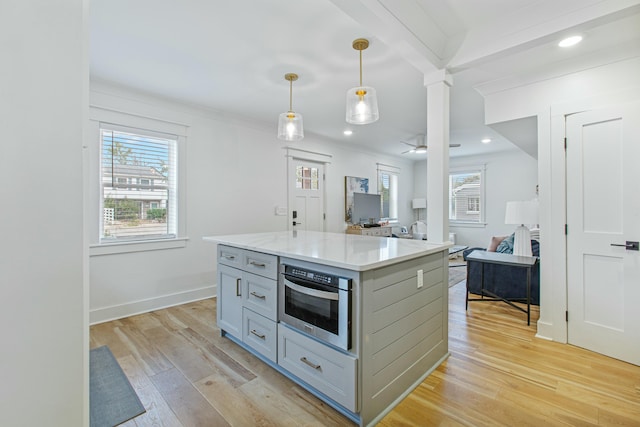 kitchen featuring light stone countertops, oven, decorative light fixtures, a kitchen island, and light wood-type flooring