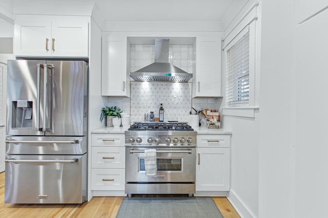 kitchen featuring wall chimney exhaust hood, premium appliances, white cabinetry, and tasteful backsplash