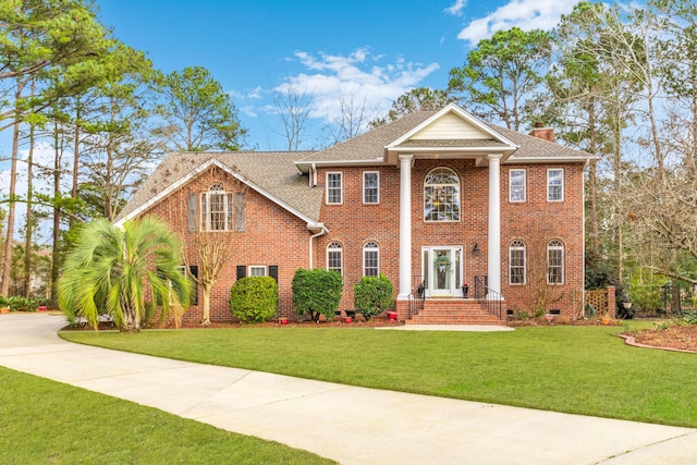 greek revival inspired property featuring a shingled roof, brick siding, a chimney, and a front lawn