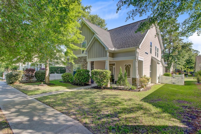 craftsman-style home featuring board and batten siding, fence, a front lawn, a shingled roof, and stone siding