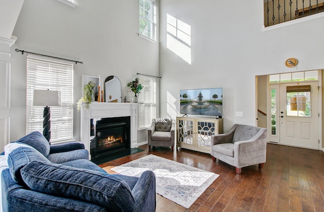 living room featuring dark wood-style flooring, a glass covered fireplace, and a towering ceiling