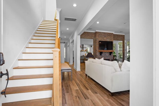 stairs featuring hardwood / wood-style floors, crown molding, brick wall, and a brick fireplace