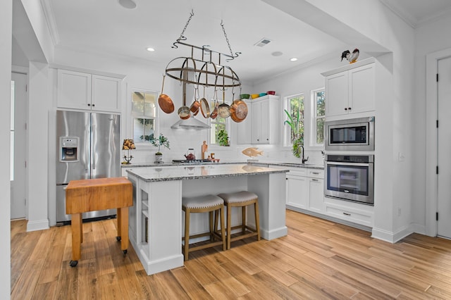 kitchen with a center island, white cabinets, hanging light fixtures, appliances with stainless steel finishes, and light stone counters