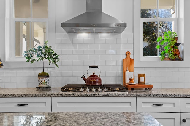 kitchen featuring white cabinets, backsplash, stainless steel gas stovetop, and wall chimney range hood