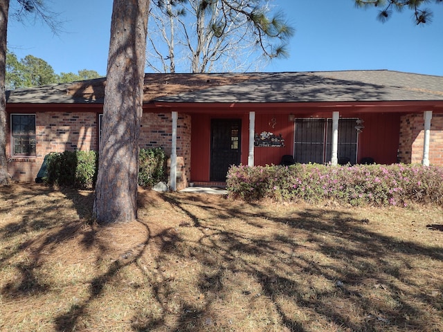 view of front of property featuring brick siding and roof with shingles