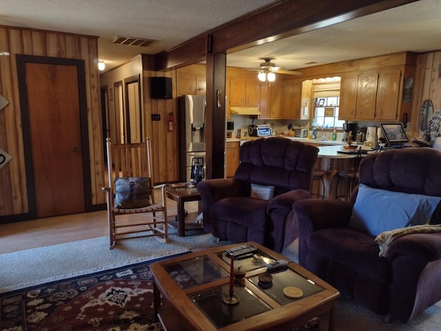 living area with visible vents, wooden walls, ceiling fan, light wood-style flooring, and a textured ceiling