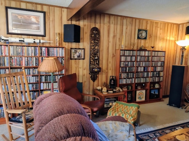 sitting room with bookshelves, carpet flooring, wood walls, and beamed ceiling