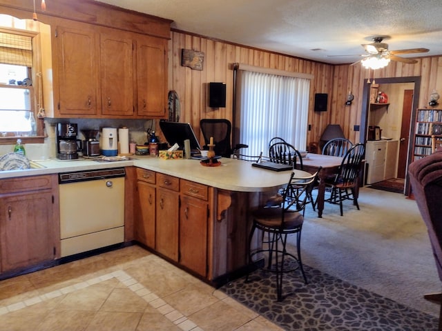 kitchen featuring a breakfast bar, a peninsula, white dishwasher, light countertops, and brown cabinets