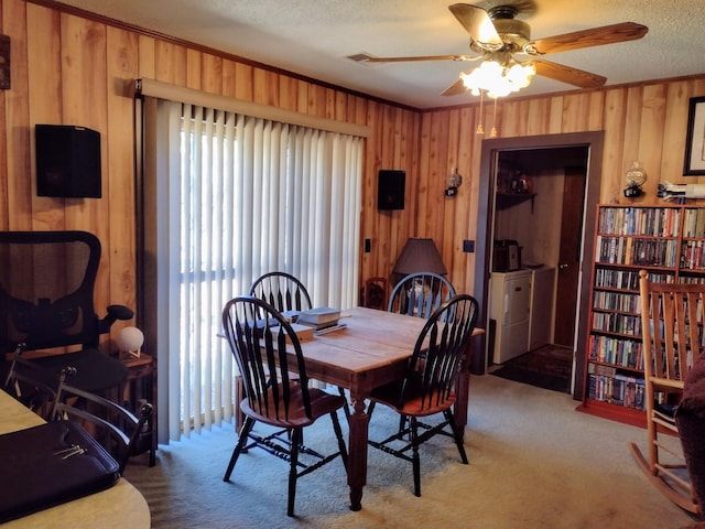 carpeted dining space with ornamental molding, a ceiling fan, a textured ceiling, wooden walls, and washer / dryer