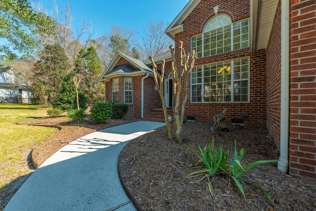 property entrance featuring crawl space, brick siding, and a lawn