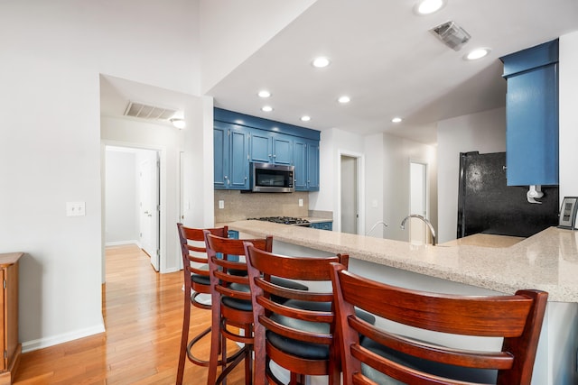 kitchen with visible vents, stainless steel microwave, freestanding refrigerator, blue cabinets, and a peninsula