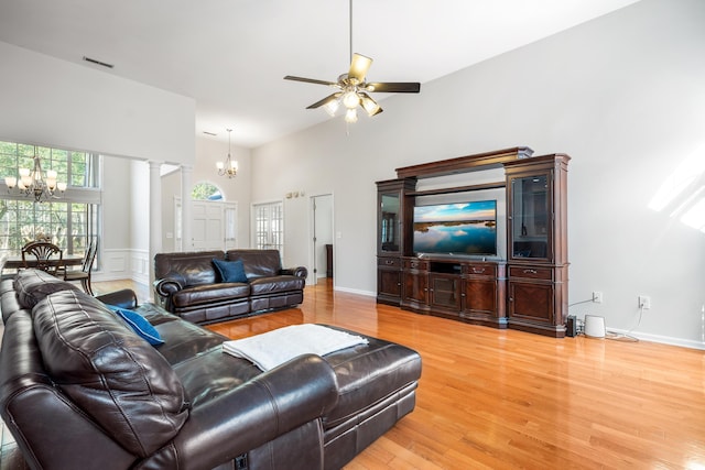 living area with ceiling fan with notable chandelier, a high ceiling, light wood-type flooring, and decorative columns