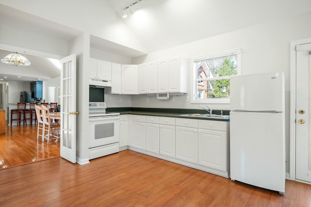 kitchen featuring under cabinet range hood, white appliances, a sink, vaulted ceiling, and dark countertops