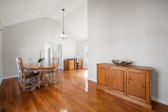 dining room featuring light wood-style flooring, high vaulted ceiling, and baseboards