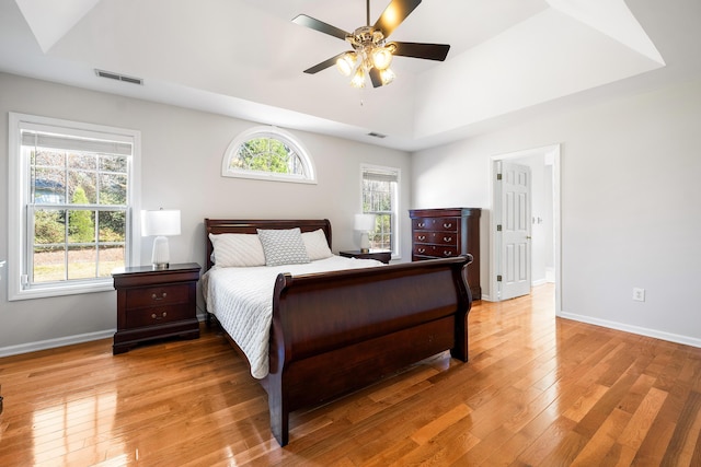 bedroom with visible vents, baseboards, vaulted ceiling, light wood finished floors, and a raised ceiling