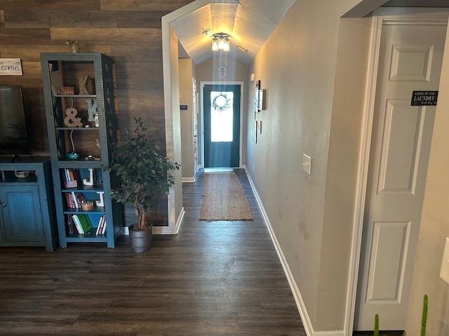 foyer entrance featuring vaulted ceiling, dark wood-type flooring, and wood walls