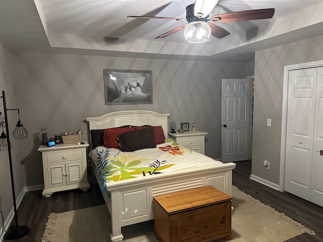 bedroom featuring dark wood-type flooring, ceiling fan, a closet, and a raised ceiling