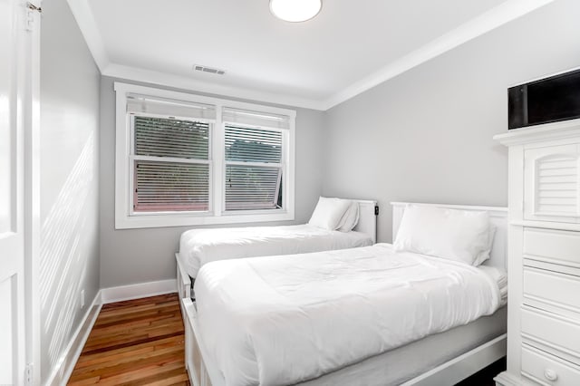 bedroom with visible vents, crown molding, baseboards, and wood finished floors