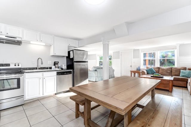 kitchen with light tile patterned floors, stainless steel appliances, white cabinets, a sink, and under cabinet range hood