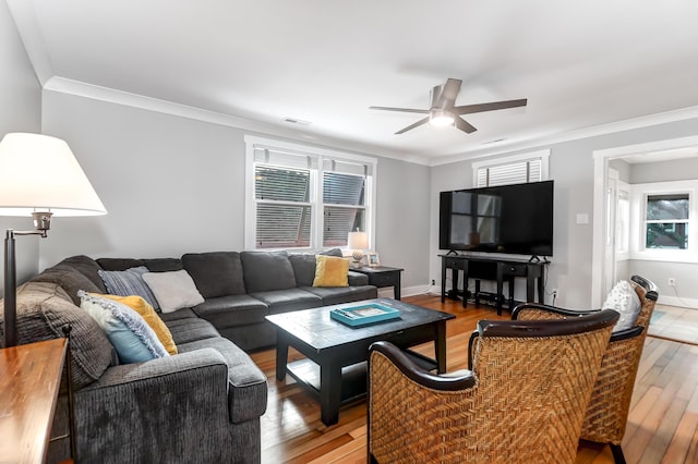 living room featuring light wood-style flooring, a ceiling fan, baseboards, visible vents, and crown molding