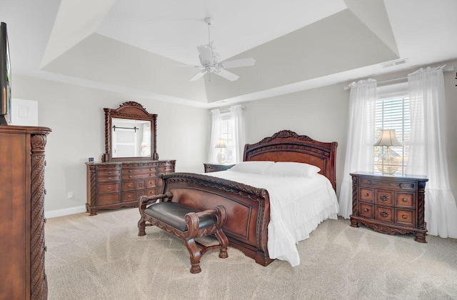 carpeted bedroom with ceiling fan, a tray ceiling, and multiple windows